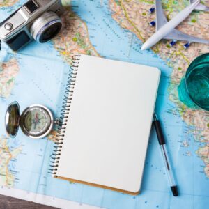 Notebook, camera, plane, pen and a compass on a map
