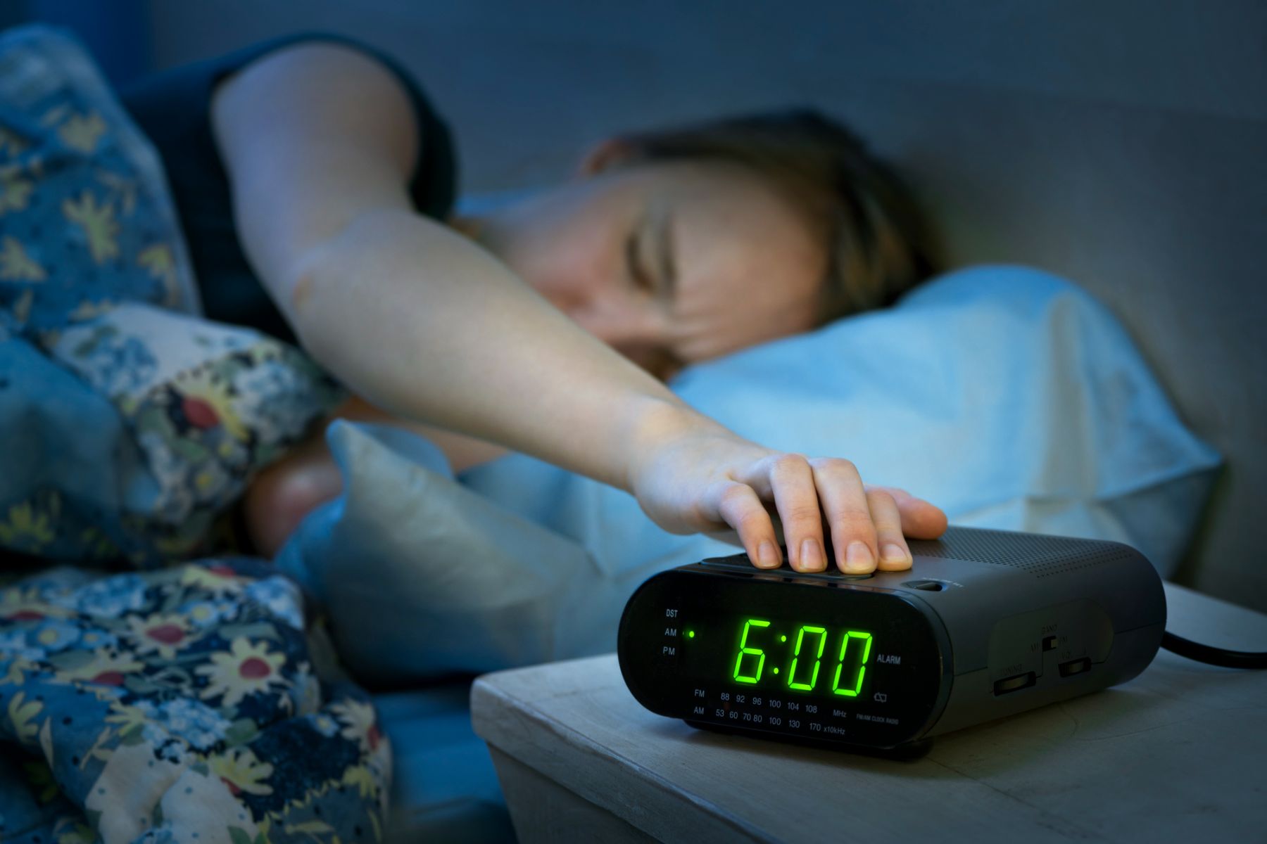 woman turning alarm clock off as she wakes up